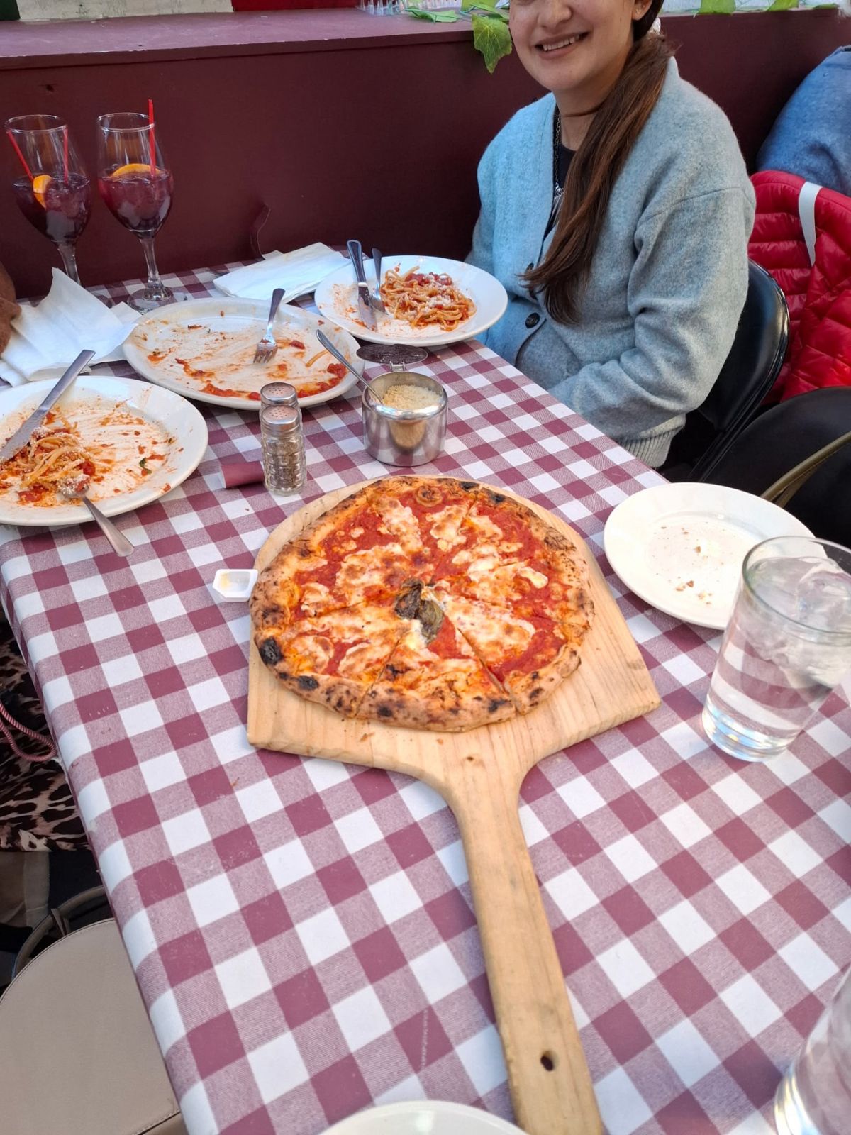 Pizza and plates of food on a red checkered table with a diner seated behind them
