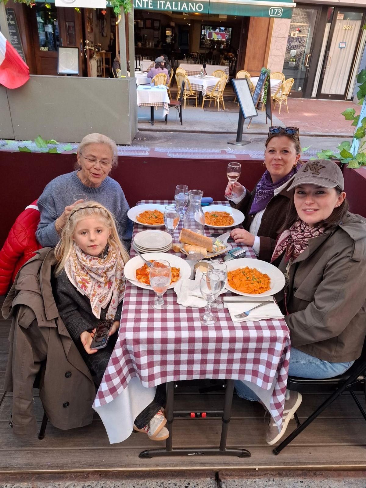 A family sharing pasta, bread and drinks at a checkered table on the outdoor terrace